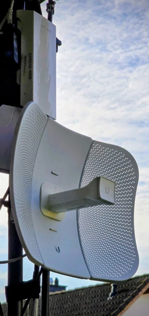 An einem Mast vor blauem Himmel: oben ein weißer TP-Link CPE510, darunter die weiße Parabolantenne eines Ubiquiti LiteBeam M5.