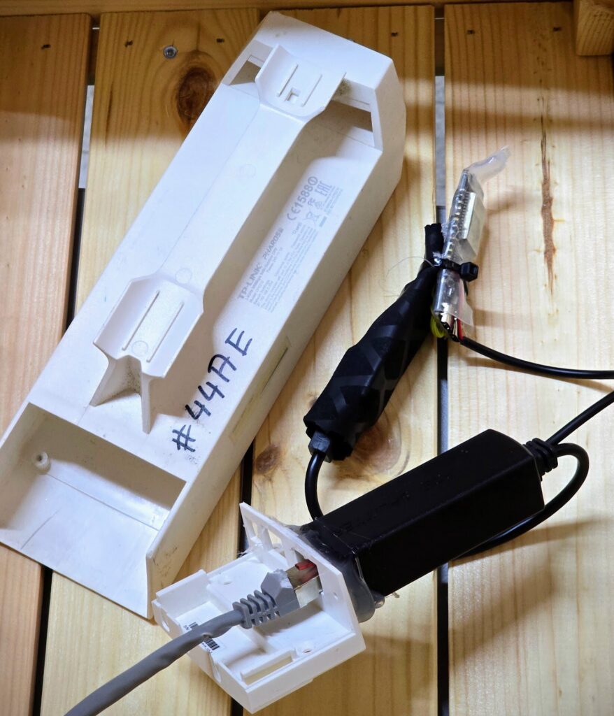 Das ausgeräumte weiße Gehäuse einer TP-Link CPE210 mit der Aufschrift #44AE, daneben die Elektronik des Empfängers mit Schrumpfschlauch und ein graues Netzwerkkabel.