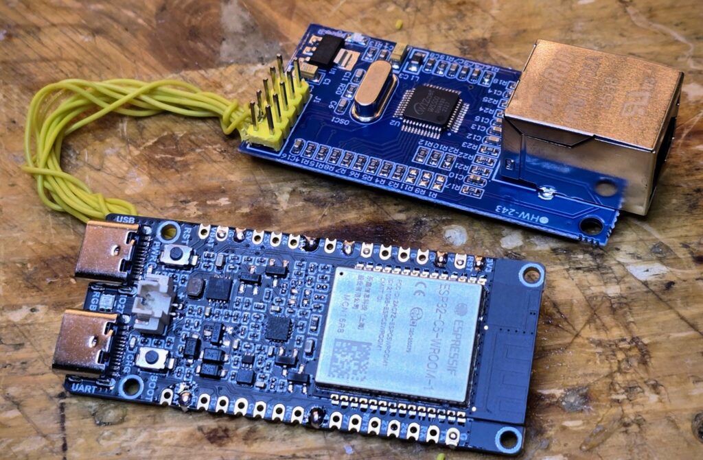 Die beiden Platinen des Empfängers auf einem Holzbrett: oben die Netzwerk-Platine mit Buchse, unten das ESP32-C5-Board, verbunden über gelbe Litzen.