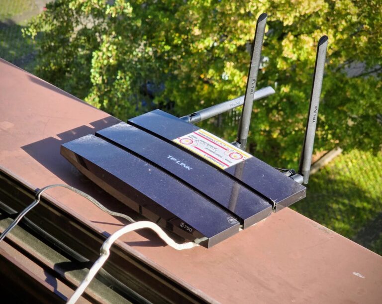 Ein schwarzer TP-Link-Router TL-WDR4300 mit drei Antennen steht auf einer Fensterbank im Freien, im Hintergrund Bäume. Oben auf dem Gehäuse ein alter, gelb-weißer Freifunk-Aufkleber.
